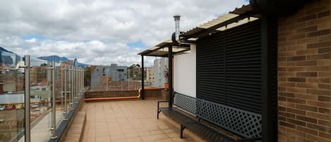 Un balcón con suelo de baldosas, un banco de metal y vistas de la ciudad.