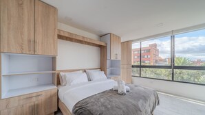 Una camera da letto moderna con un letto grande, mobili in legno e vista sugli edifici attraverso ampie finestre.