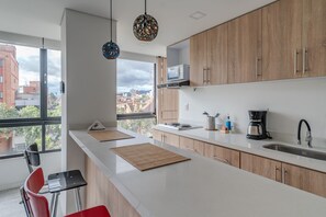 Una cocina moderna con un ventanal grande, armarios de madera, una encimera blanca y una cafetera.
