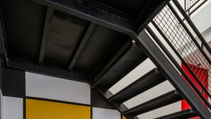 Una scala con ringhiera in metallo e un muro decorato con un motivo geometrico composto da quadrati bianchi, gialli, blu e rossi.