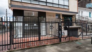 Un edificio con recinzione in metallo nero, vialetto in mattoni e una scalinata che conduce a una porta con su scritto "ATARDECER 57".
