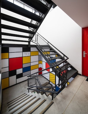 Una scala con ringhiera in metallo nero e un muro colorato con motivi geometrici.