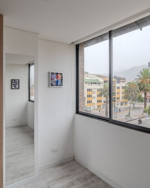 A narrow hallway with a large window, white walls, and a view of a cityscape with buildings and palm trees.