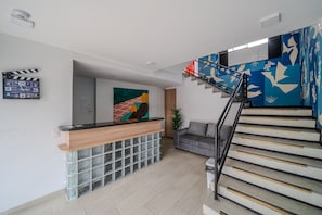 A modern interior with a reception desk, a staircase with a blue and white design, and a grey sofa.
