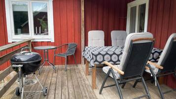 An outdoor patio with a barbecue grill, two chairs, and a table with a patterned tablecloth.