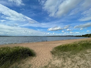 Ein Strand mit einem sandigen Pfad, der zum Wasser führt, umgeben von grünen Flächen.