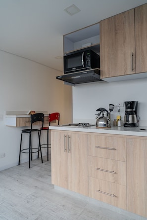 Een moderne keuken met houten kastjes, een magnetron, een waterkoker en een koffiezetapparaat.