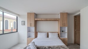 A modern bedroom with a large bed, wooden cabinets, and a view of a building with arches through a large window. - Nice Loft @Chapinero close to Movistar Arena (Bogotá)