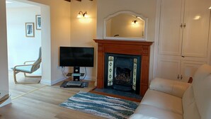 Een woonkamer met een open haard, een televisie, een bank en een fauteuil.