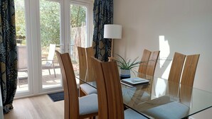 Een eetgedeelte met een glazen tafel, houten stoelen en een potplant.
