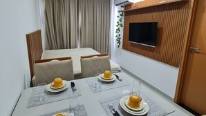 A modern dining area with a table set for four, a sofa, and a TV mounted on the wall. - Flat 104A no Bela Vista by La Playa  (Ipojuca)