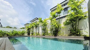 A swimming pool with clear blue water, surrounded by lush greenery and modern buildings. - laguna 5 卧室，私人泳池别墅 (Tambon Choeng Thale)
