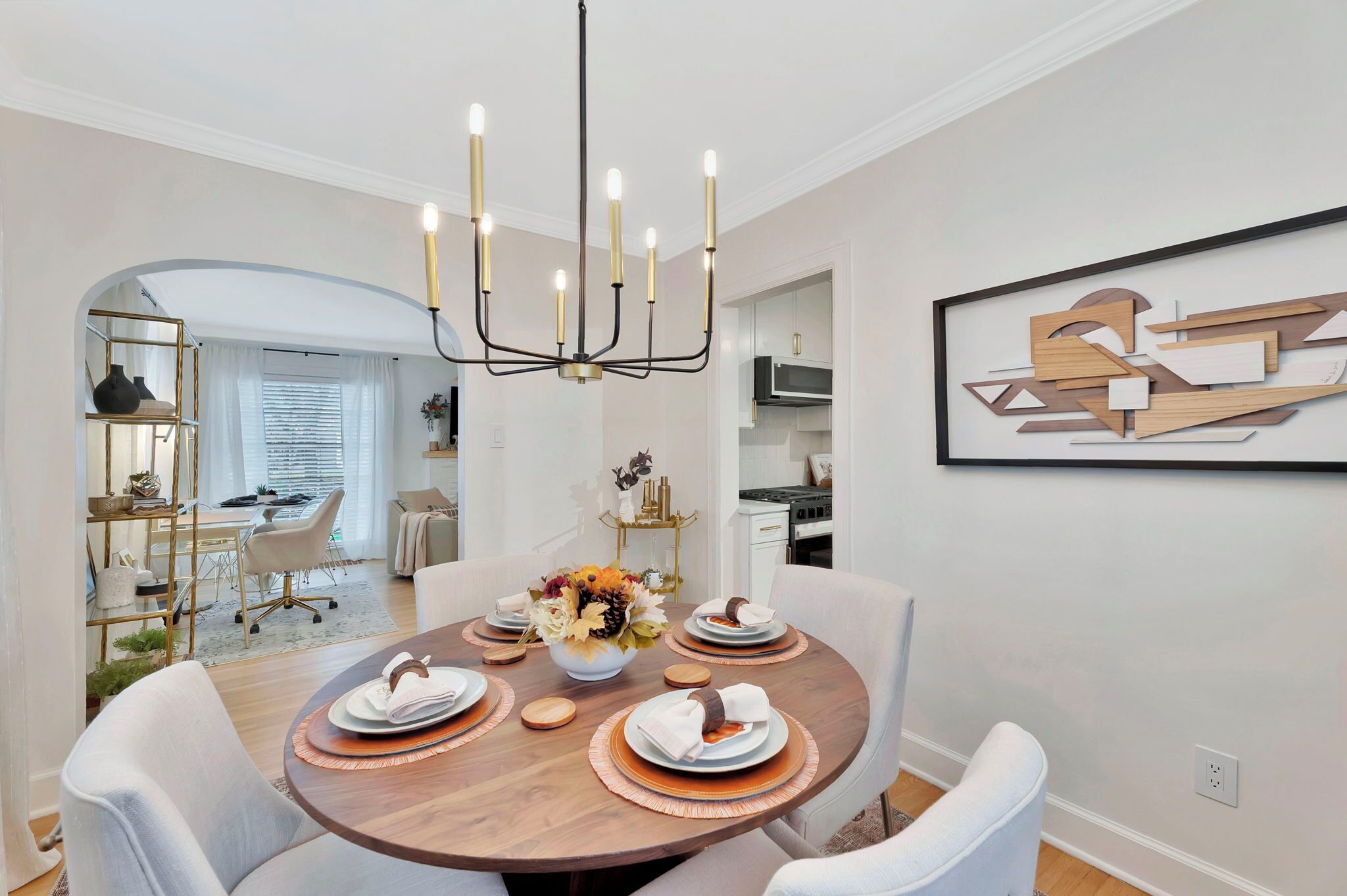 A dining room with a round table set for four, a chandelier, and a framed abstract painting on the wall.