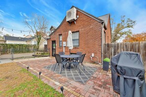 Une terrasse avec une table et des chaises, un barbecue et une maison en briques.