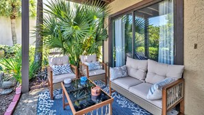 A covered outdoor seating area with a glass table, cushioned chairs, and a sofa. - Portside I1- Gulf Palms (Panama City Beach)