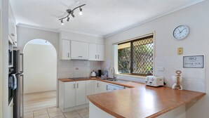 A modern kitchen with white cabinets, a wooden countertop, a window with a view, a clock, and a sign reading "BBQ THANK YOU". - Family & Pet friendly Beachside with AC (Minyama)