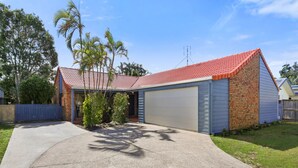 A single-story house with a red-tiled roof, a garage, and a small front yard with a concrete driveway. - Family & Pet friendly Beachside with AC (Minyama)