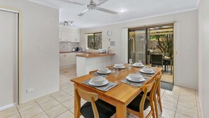 A modern kitchen with white cabinets, a dining area with a wooden table set for four, and a sliding glass door leading to an outdoor patio. - Family & Pet friendly Beachside with AC (Minyama)