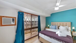 A bedroom with a bed, a ceiling fan, a window with blue curtains, and an air conditioning unit. - Family & Pet friendly Beachside with AC (Minyama)