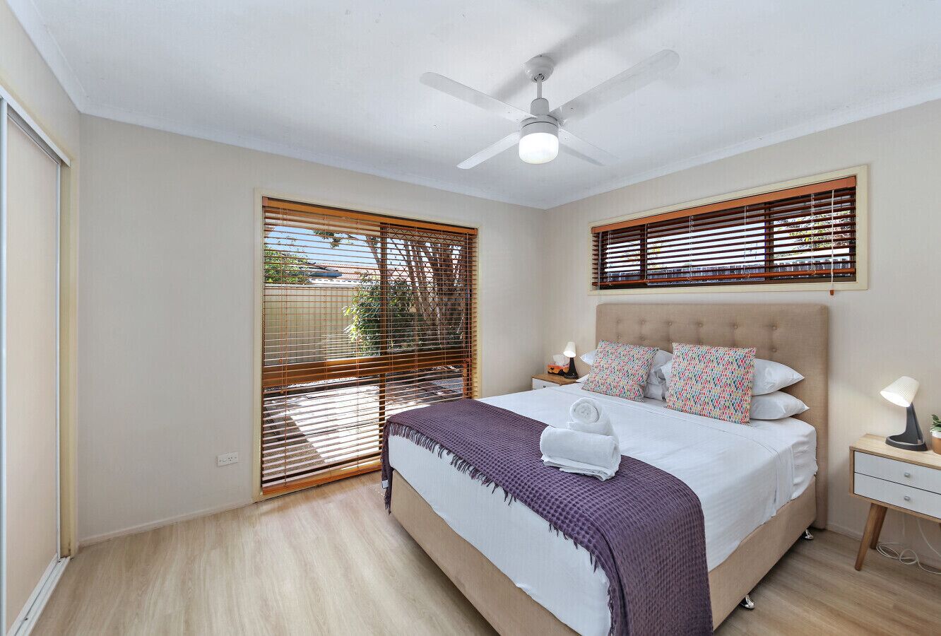 A bedroom with a bed, a ceiling fan, a nightstand, and a window with blinds.
