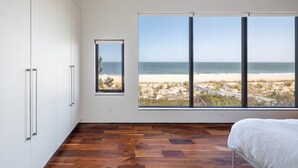A bedroom with a large window offering a beach view, wooden flooring, and white walls. - Oceanview 5-BR House in Bethany Beach w/ Elevator (Bethany Beach)