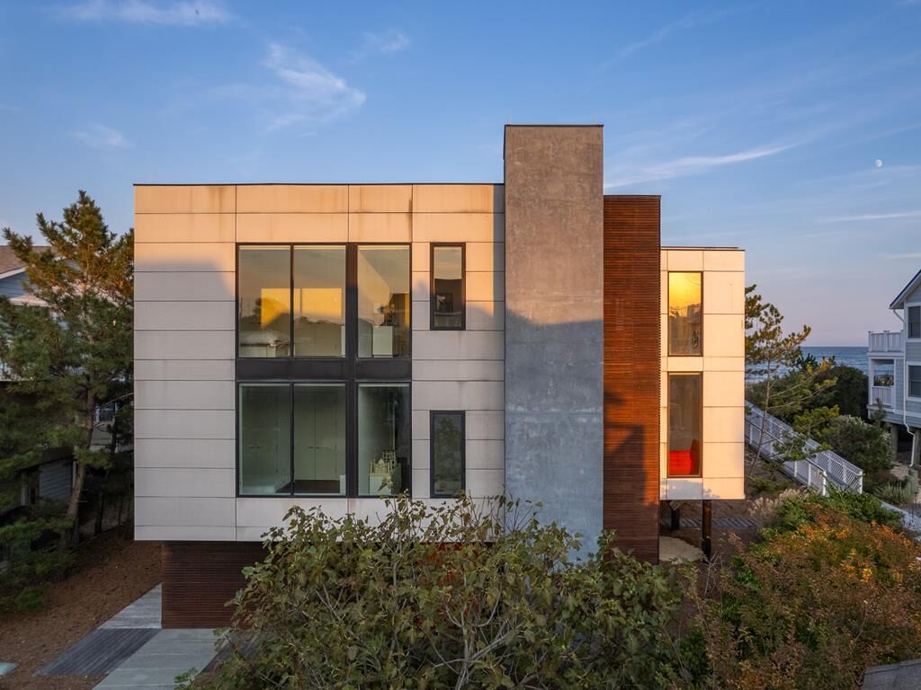 A modern two-story house with large windows and a prominent central chimney.