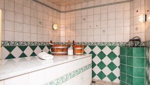 A bathroom with a white vanity, green and white patterned tiles, a towel, and a wooden bucket.