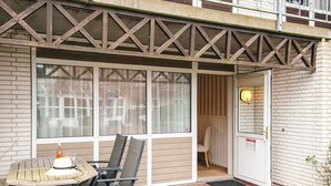 An outdoor seating area with a table and chairs, a door with a bell, and a window with curtains.