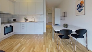 Cuina moderna amb armaris blancs, microones i forn integrat. Hi ha una zona de menjador amb taula i cadires.