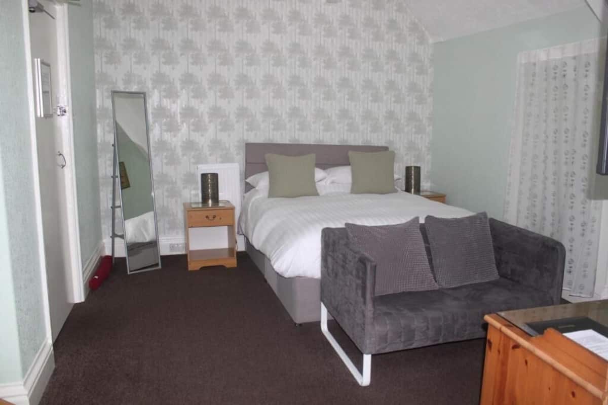A bedroom with a bed, a nightstand, a mirror, a sofa, and a wooden dresser.