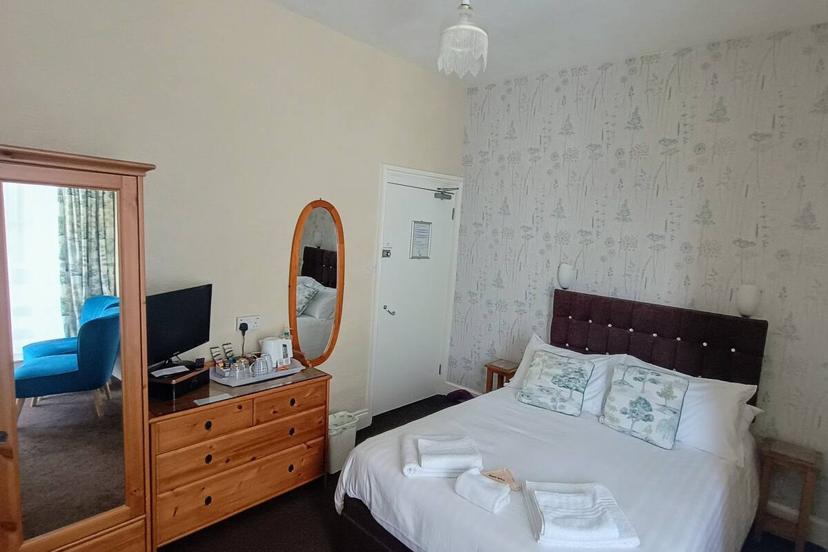 A hotel room with a bed, a dresser, a mirror, a television, and a wardrobe.