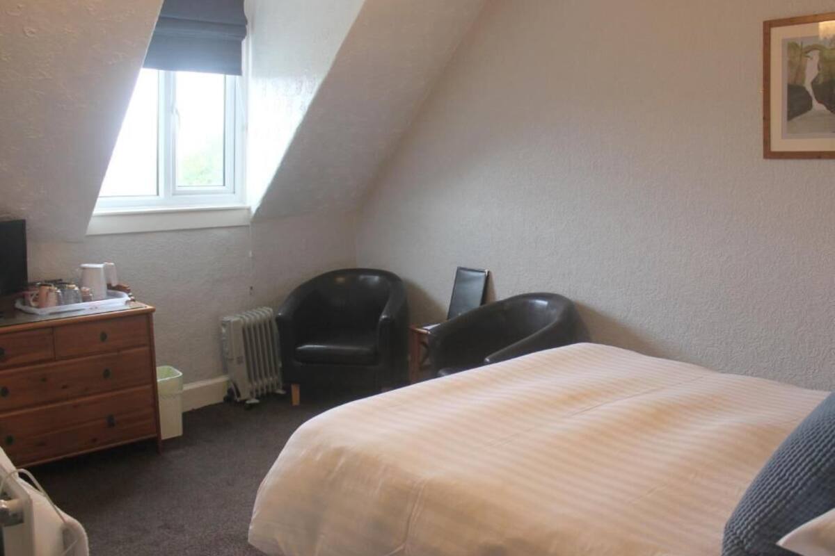 A bedroom with a bed, a dresser, a chair, a radiator, and a window.