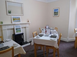 Un comedor con chimenea, cuadros en la pared y una mesa preparada para cuatro comensales.