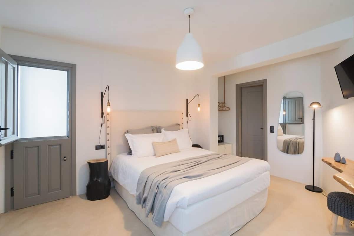 A bedroom with a large bed, bedside lamps, a mirror, and a TV mounted on the wall.