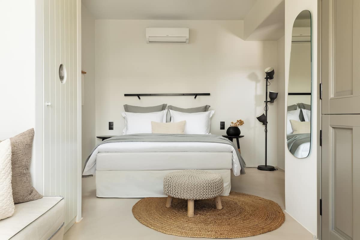 A modern bedroom with a bed, bedside tables, a floor lamp, a mirror, and a woven rug.