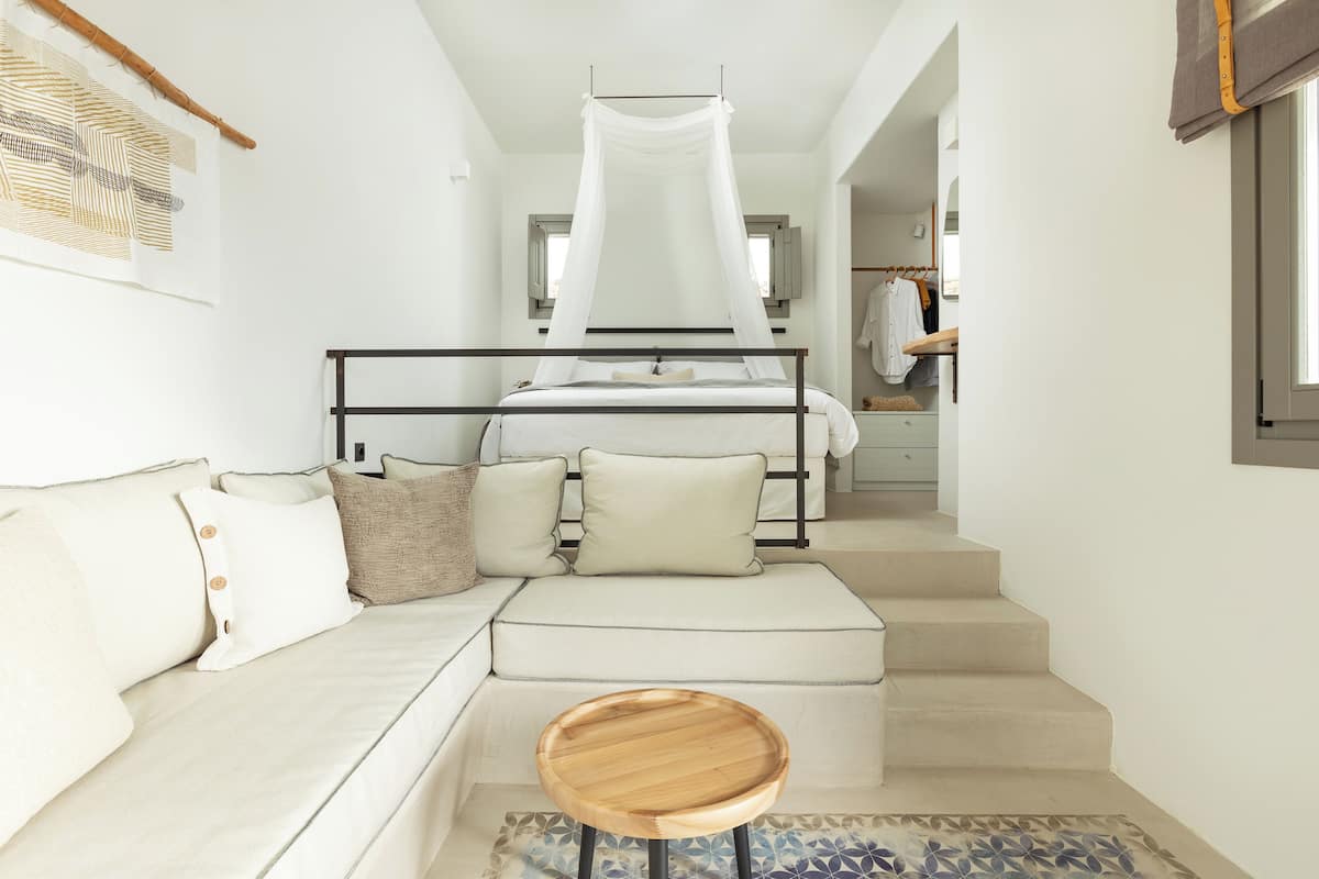 A bedroom with a bed, a sofa, a wooden stool, and a staircase leading to a bathroom.
