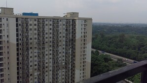 A high-rise building with multiple balconies and a view of a highway and greenery in the background. - Podomoro Golf View By Arsakha Property (Gunung Putri)
