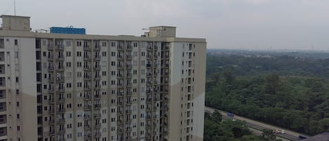 A high-rise building with multiple balconies and a view of a highway and greenery in the background.