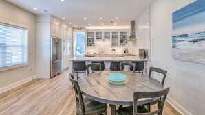 A modern kitchen with white cabinets, a central island, and a dining area with a round table and chairs.