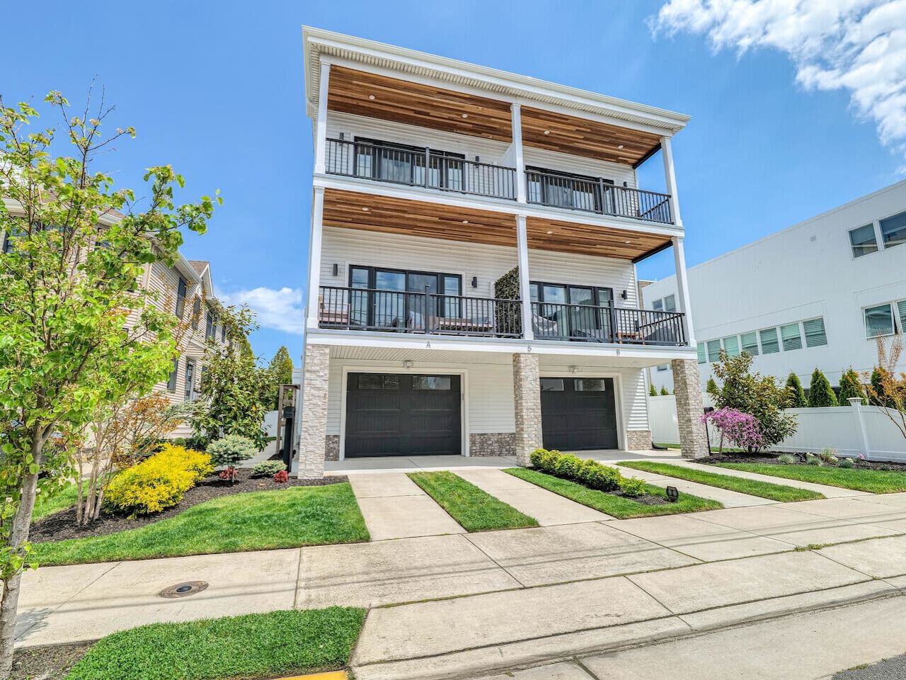 A two-story residential building with a central garage, a balcony on the upper floor, and a well-maintained front yard with grass and shrubs.