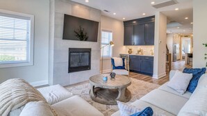 A modern living room with a fireplace, a dining area, and a kitchen.