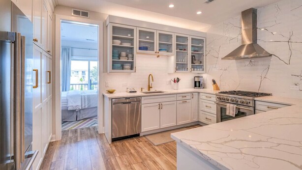 A modern kitchen with white cabinets, a stainless steel range hood, and a marble countertop.