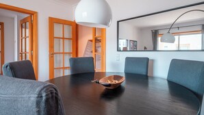 A round table with a wooden bowl and a keychain, surrounded by four chairs, in a room with wooden doors and a large mirror on the wall.