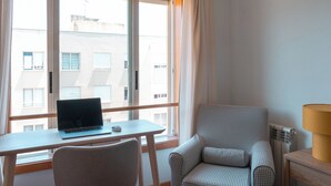 A hotel room with a desk, laptop, chair, and a lamp.