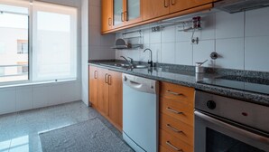 A modern kitchen with wooden cabinets, a dishwasher, an oven, and a window providing natural light.