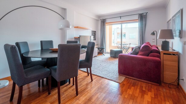A modern living room with a round dining table, grey chairs, a red sofa, and a wooden cabinet.