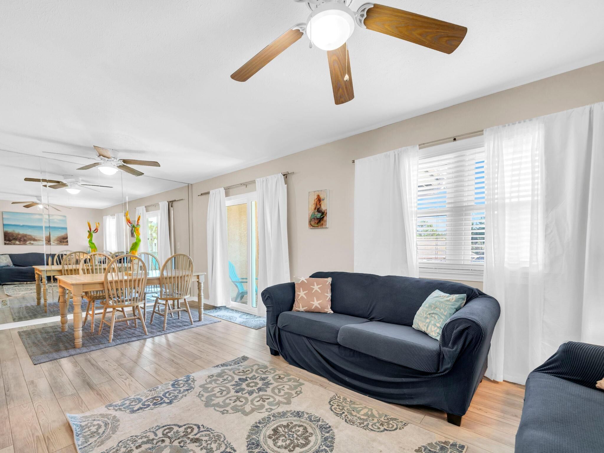 A spacious living area with a dark blue sofa, wooden dining table, and ceiling fans.