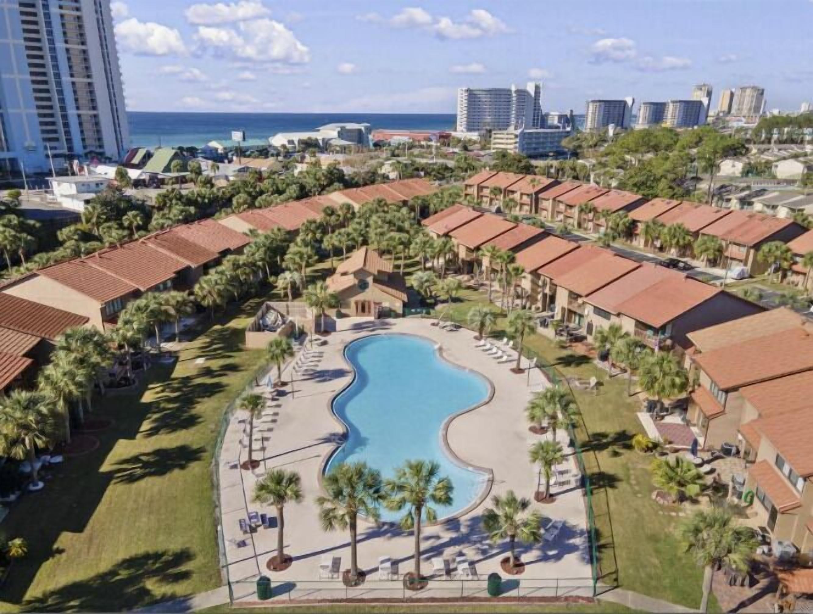 A resort with a central swimming pool, multiple bungalow-style buildings, and a view of the ocean.