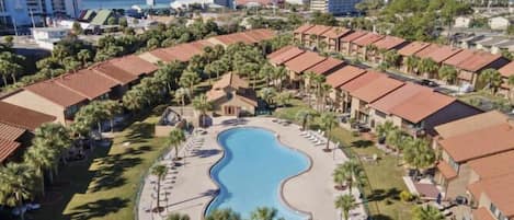 A resort with a central swimming pool, multiple bungalow-style buildings, and a view of the ocean.