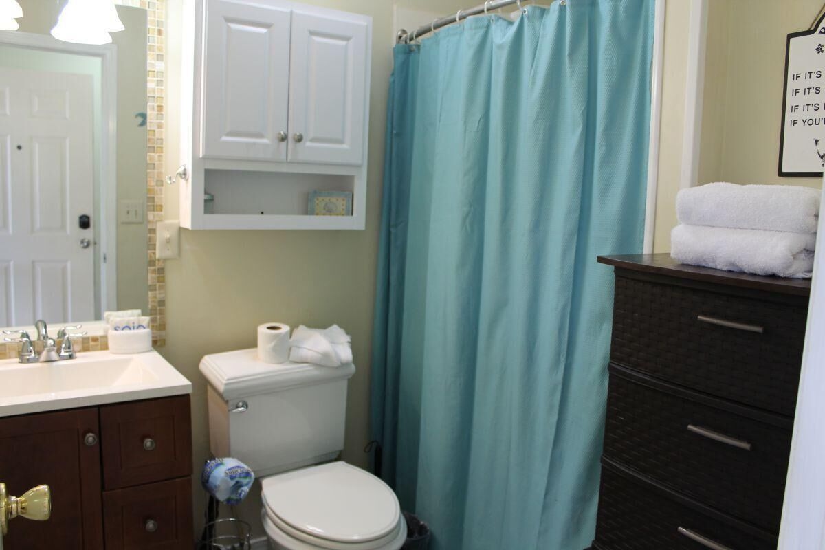 Un baño con inodoro, lavamanos, armario y cortina de ducha azul.